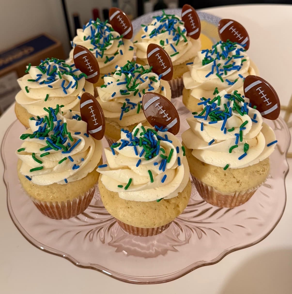 Super Bowl cupcakes with vanilla buttercream swirls, blue and green sprinkles, and chocolate football toppers