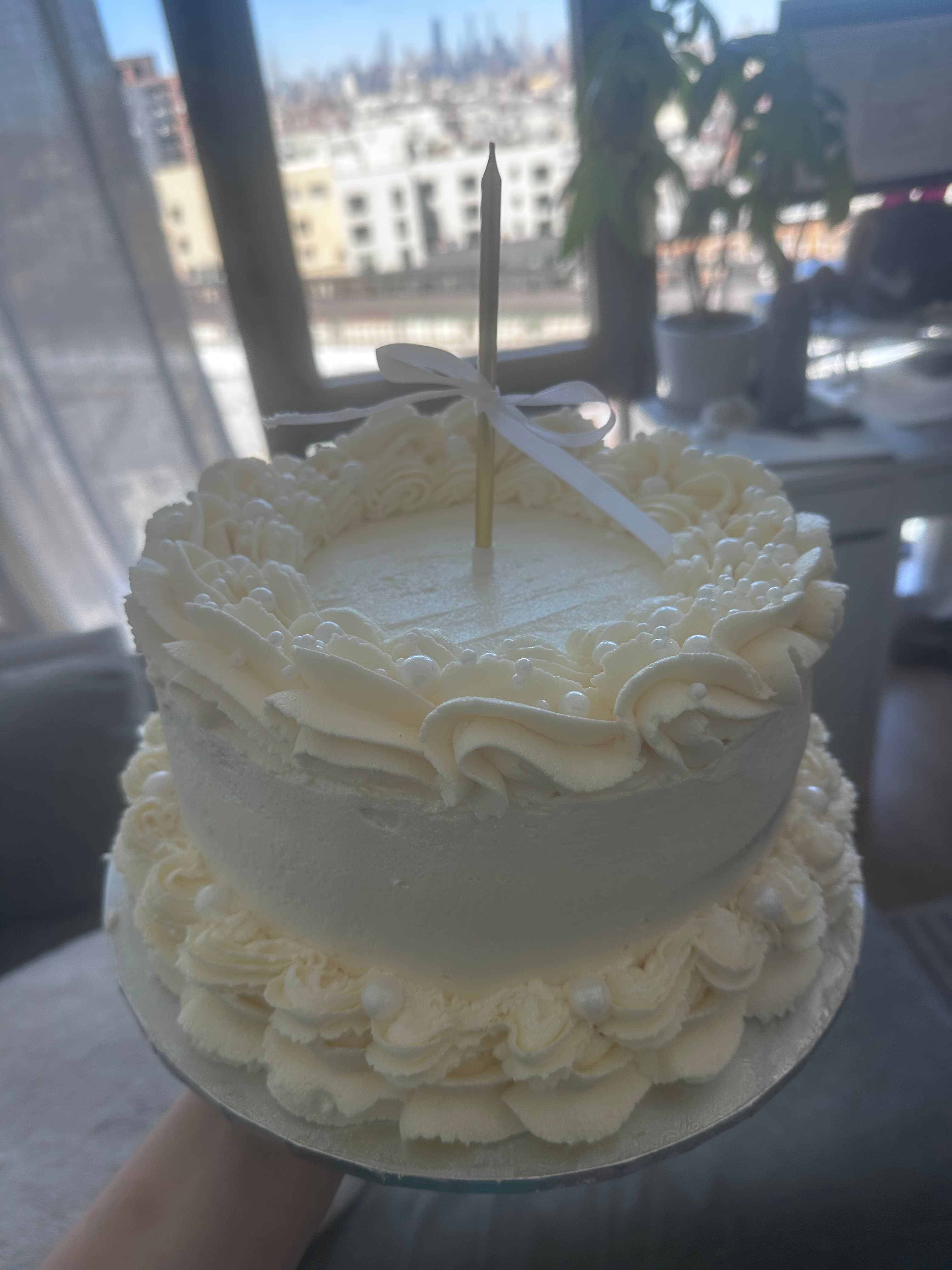 Berry chantilly birthday cake with ruffled piping, a white bow, pearl sprinkles, and a gold candle